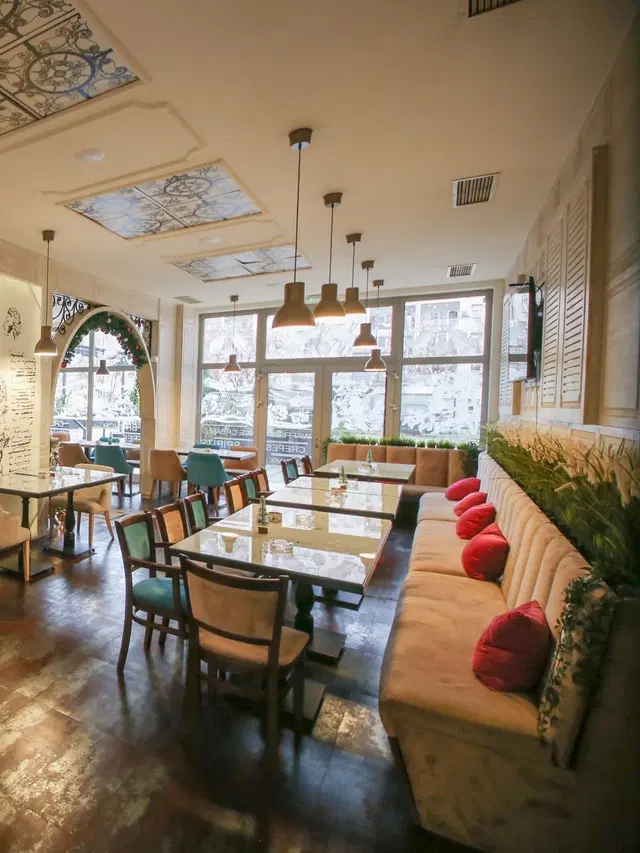 An upholstered banquette with cushions and tables by the windows at Sweet & Salty, New Belgrade